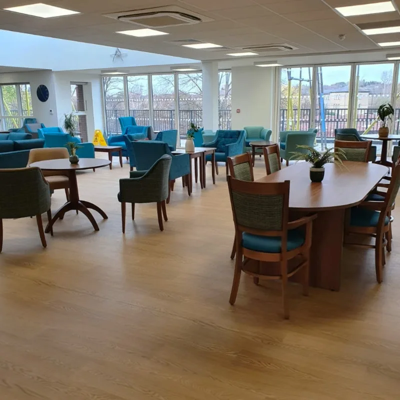An empty café dining room with teal armchairs, wooden tables and large windows